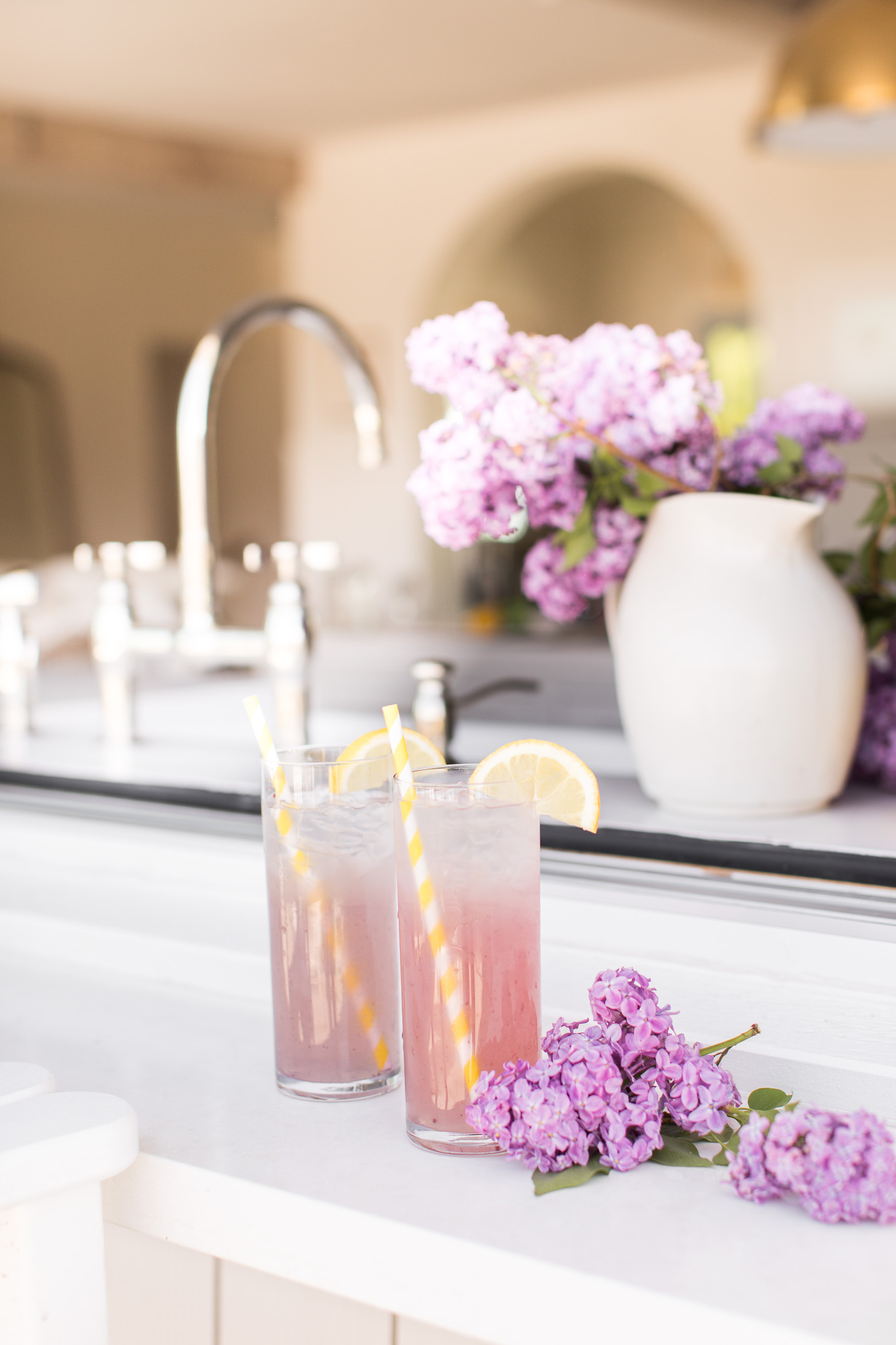 Two glasses of lemonade on the counter beside lilac clippings.