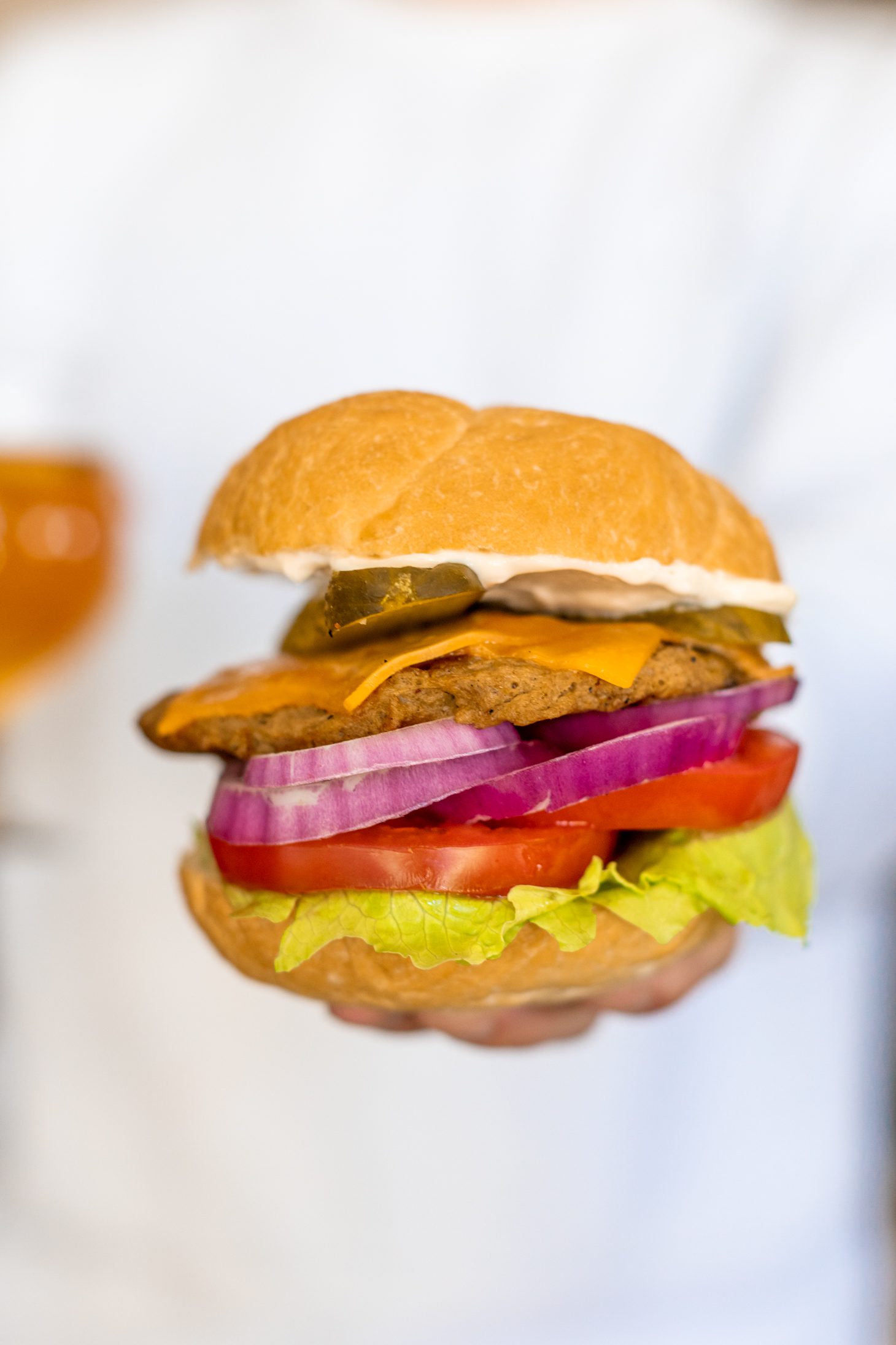 Jillian Harris holding seitan burger on a bun with lettuce, tomato, pickles, cheese, red onion and mayo.