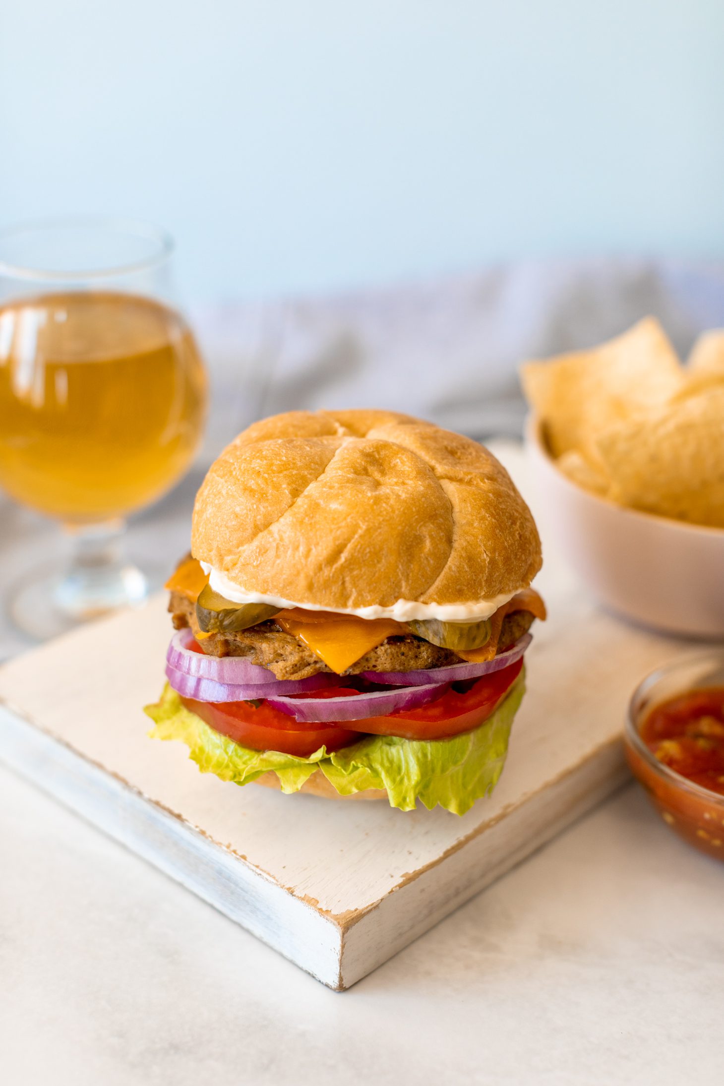 Jillian Harris' seitan burger on a bun next to tortilla chips, a bowl of salsa, and a glass of light beer.