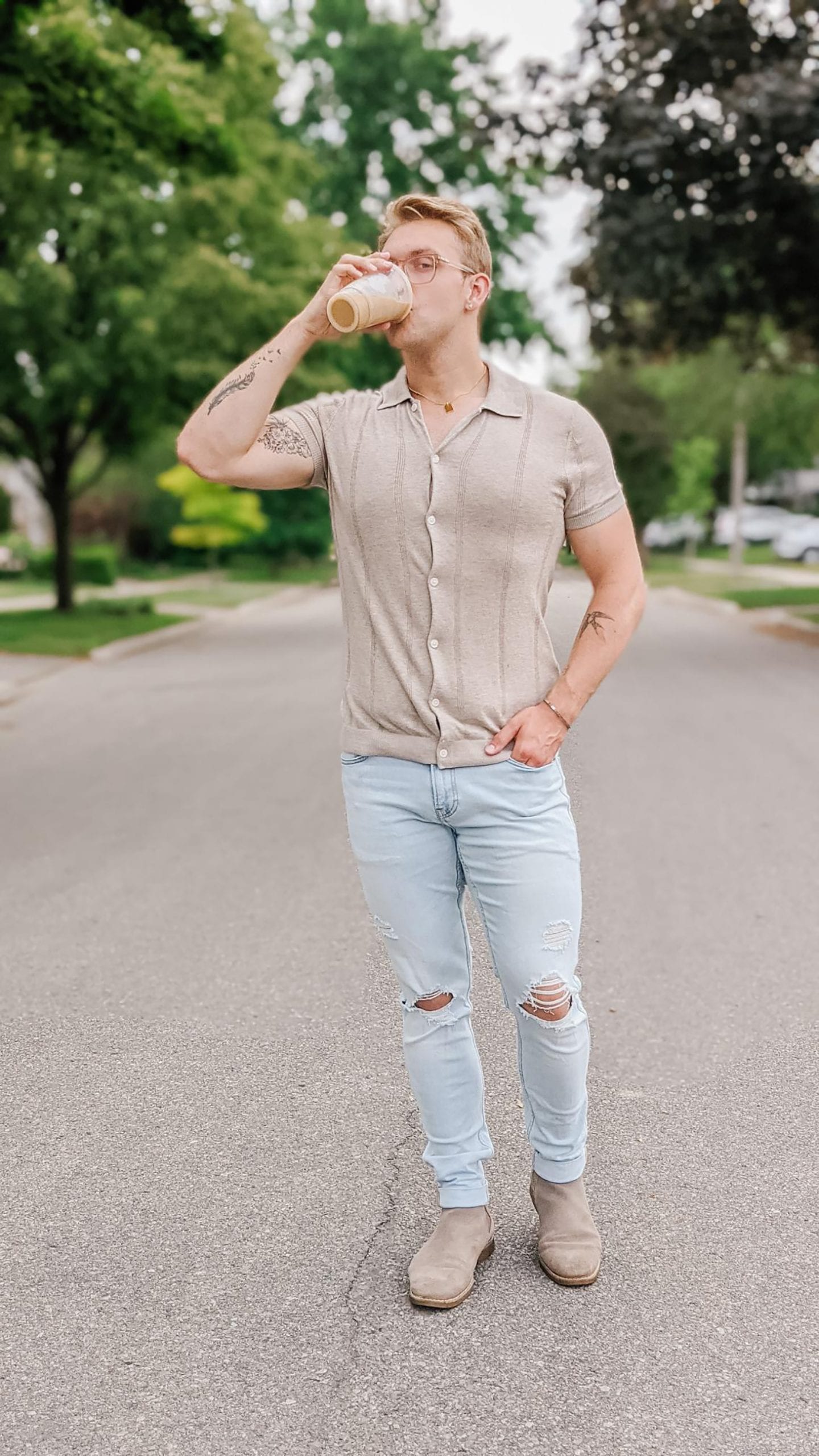 Christoper Allen standing in the middle of a residential street lined with trees, drinking coffee while showing one of his Favourite Summer Looks.