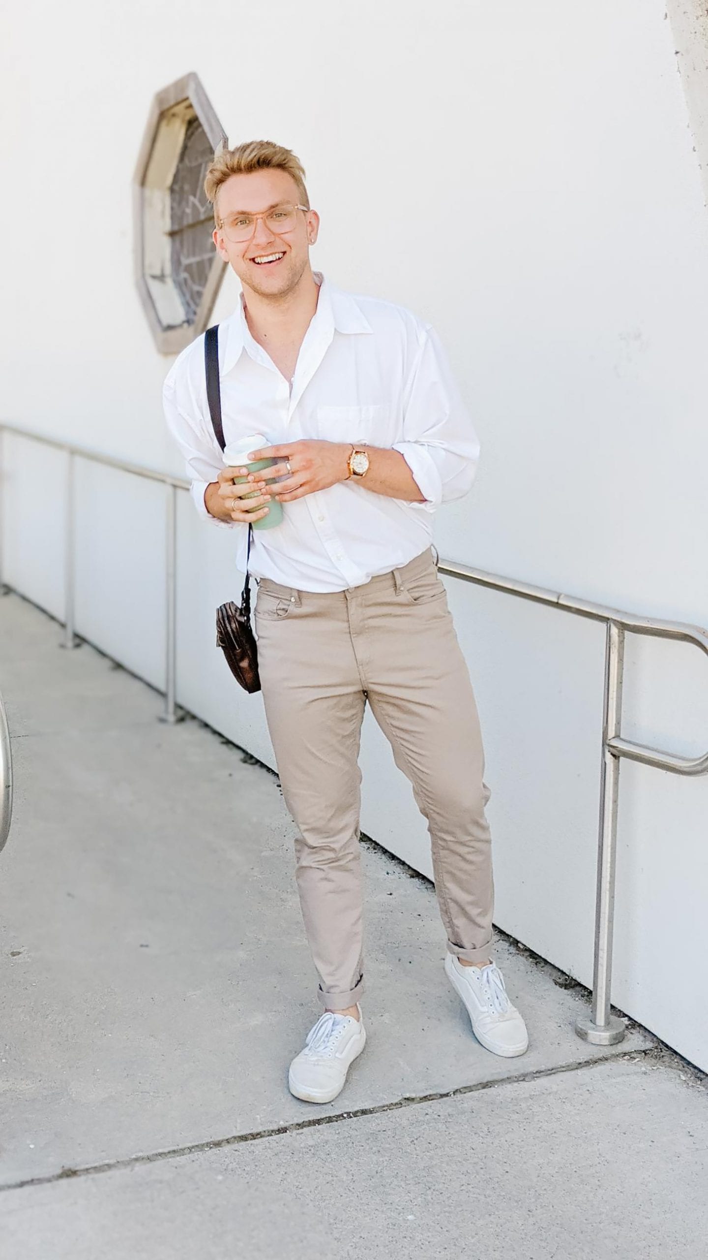 Blonde man, Christoper Allen, standing outside of a white building wearing a casual white button down shirt and tapered khaki pants. 