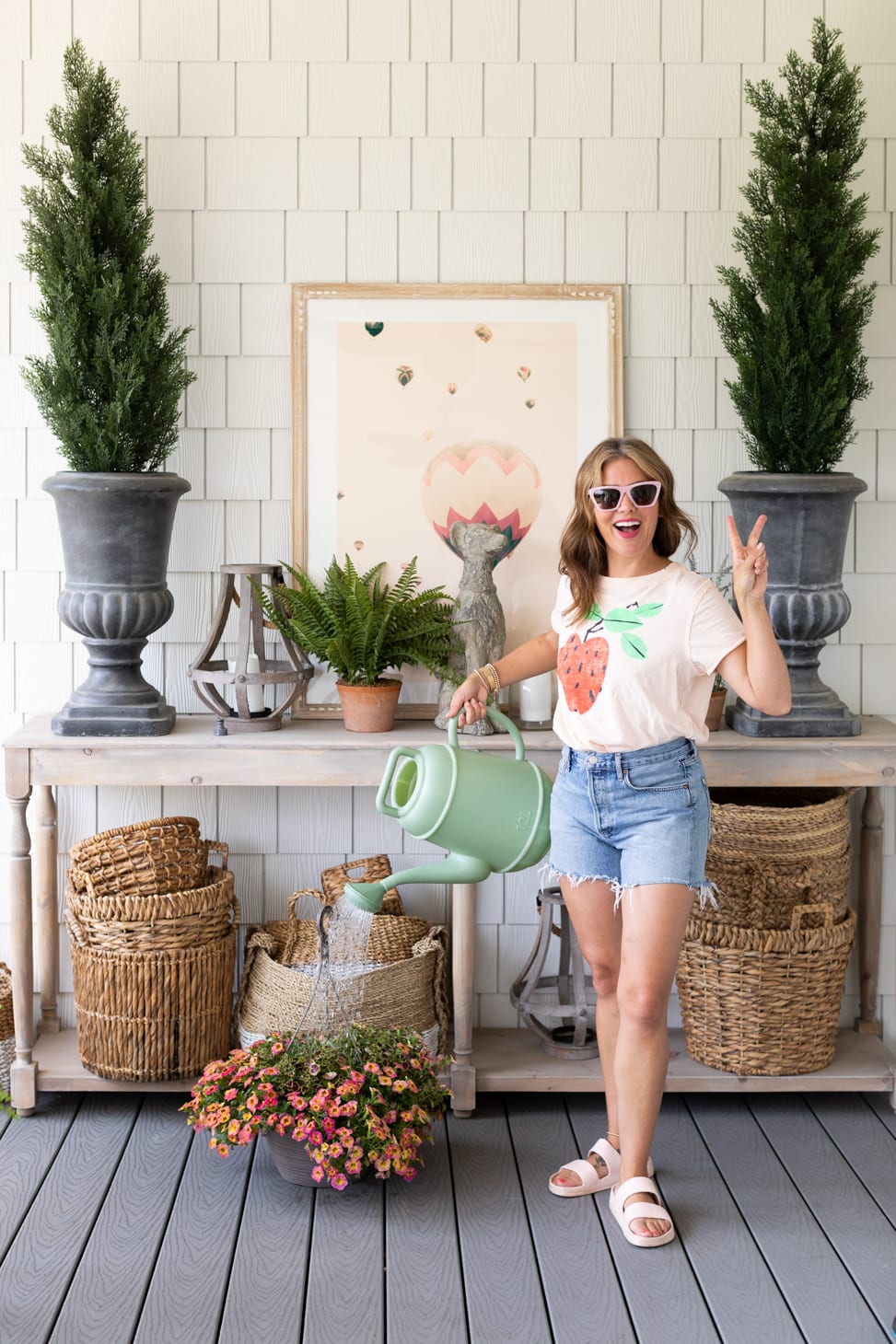 Jillian Harris watering a hanging basket of flowers on her porch wearing one of her Go-To Farm-Inspired Outfits.