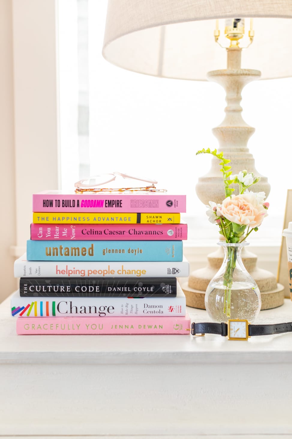 Jillian Harris's nightstand with a stack of books that encourages growth along with a lamp, flowers in a vase and watch. 