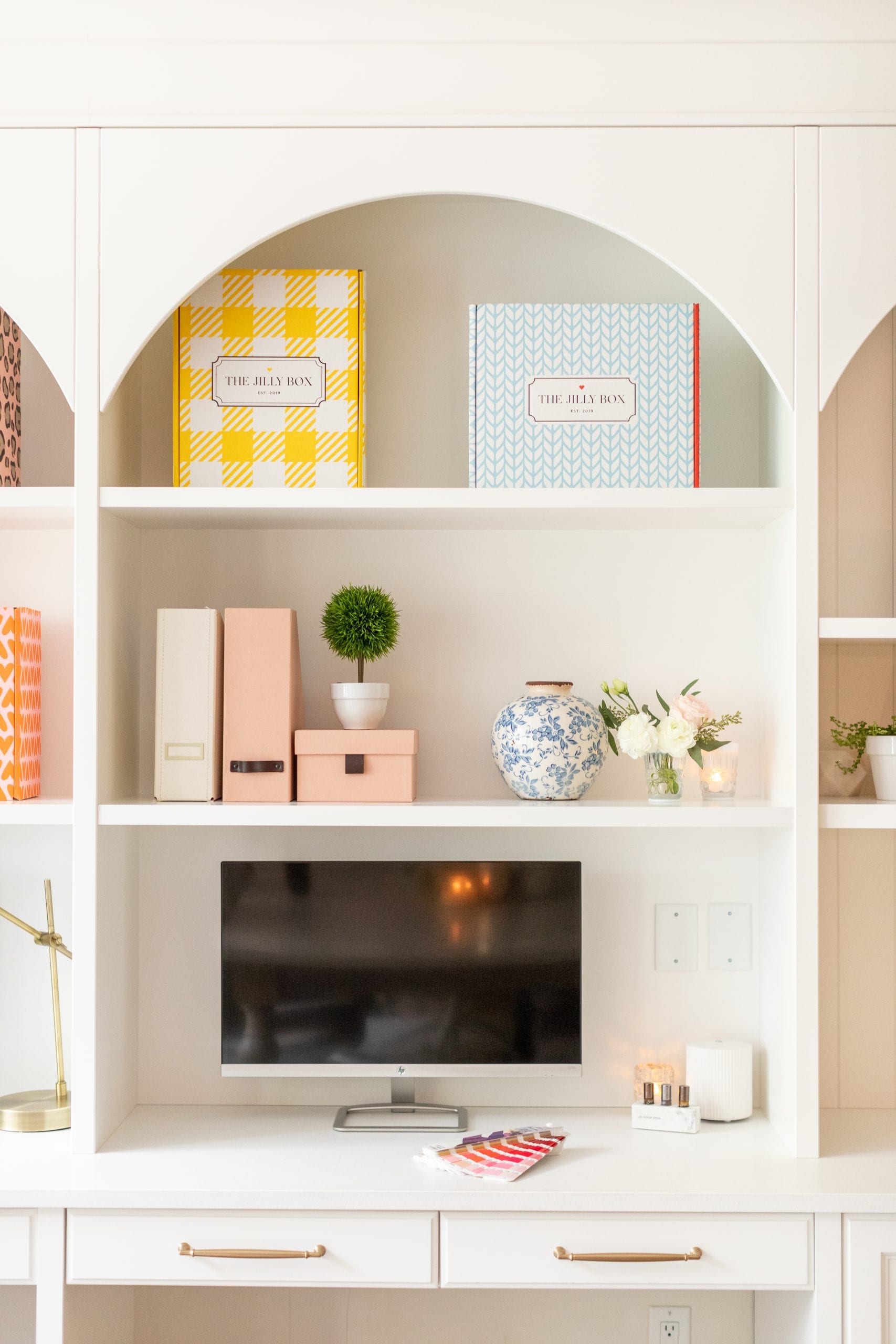 Jillian Harris' office with Jilly Boxes on the shelf, as well as decor items and computer used to watch The Jilly Academy Courses.