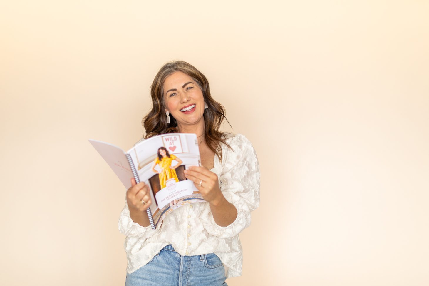 Jillian Harris on a plain backdrop with a Jilly Academy workbook ready for fall semester. 