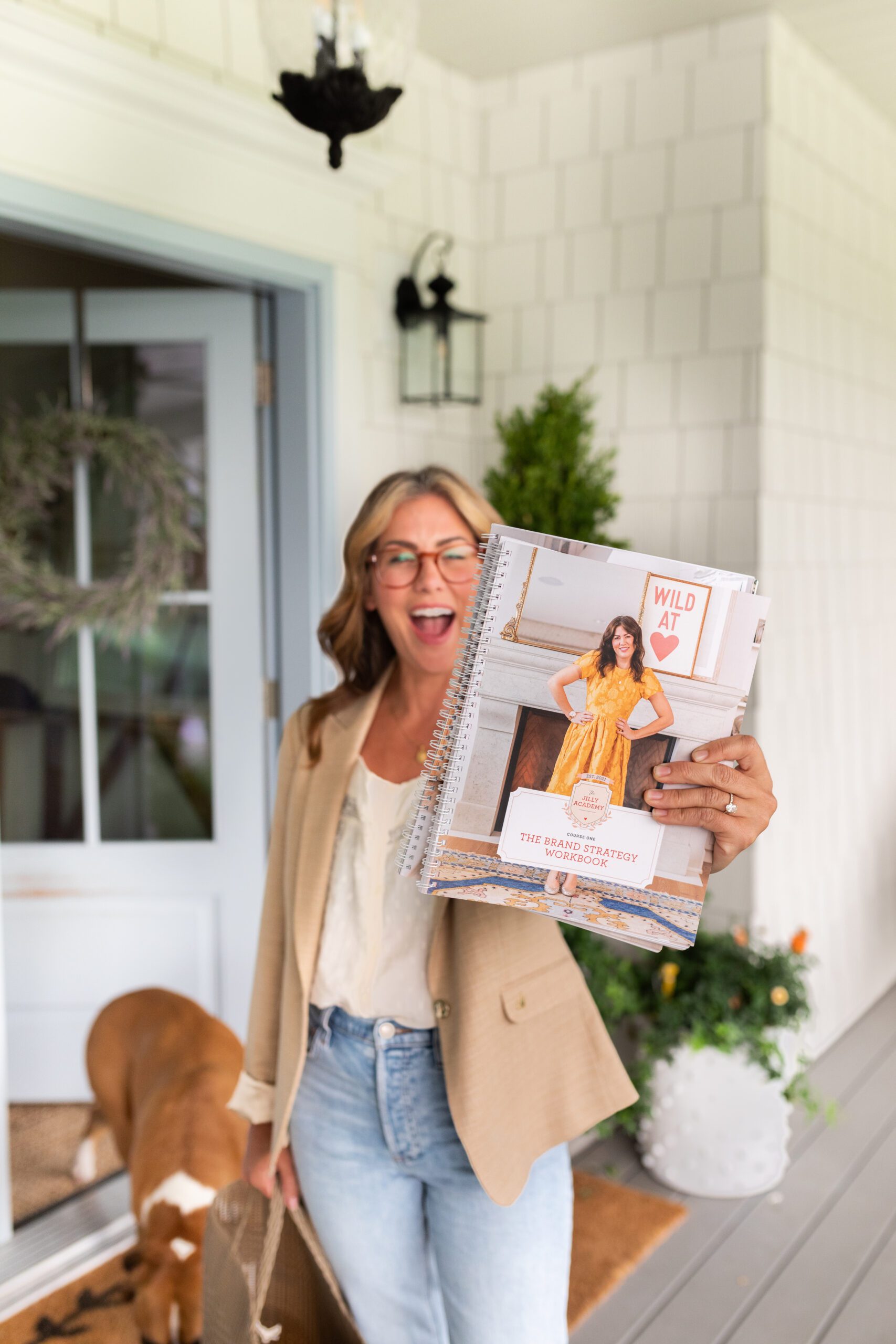 Jillian Harris on her front porch showing excitement for The Jilly Academy's Fall Semester, holding the workbook. 