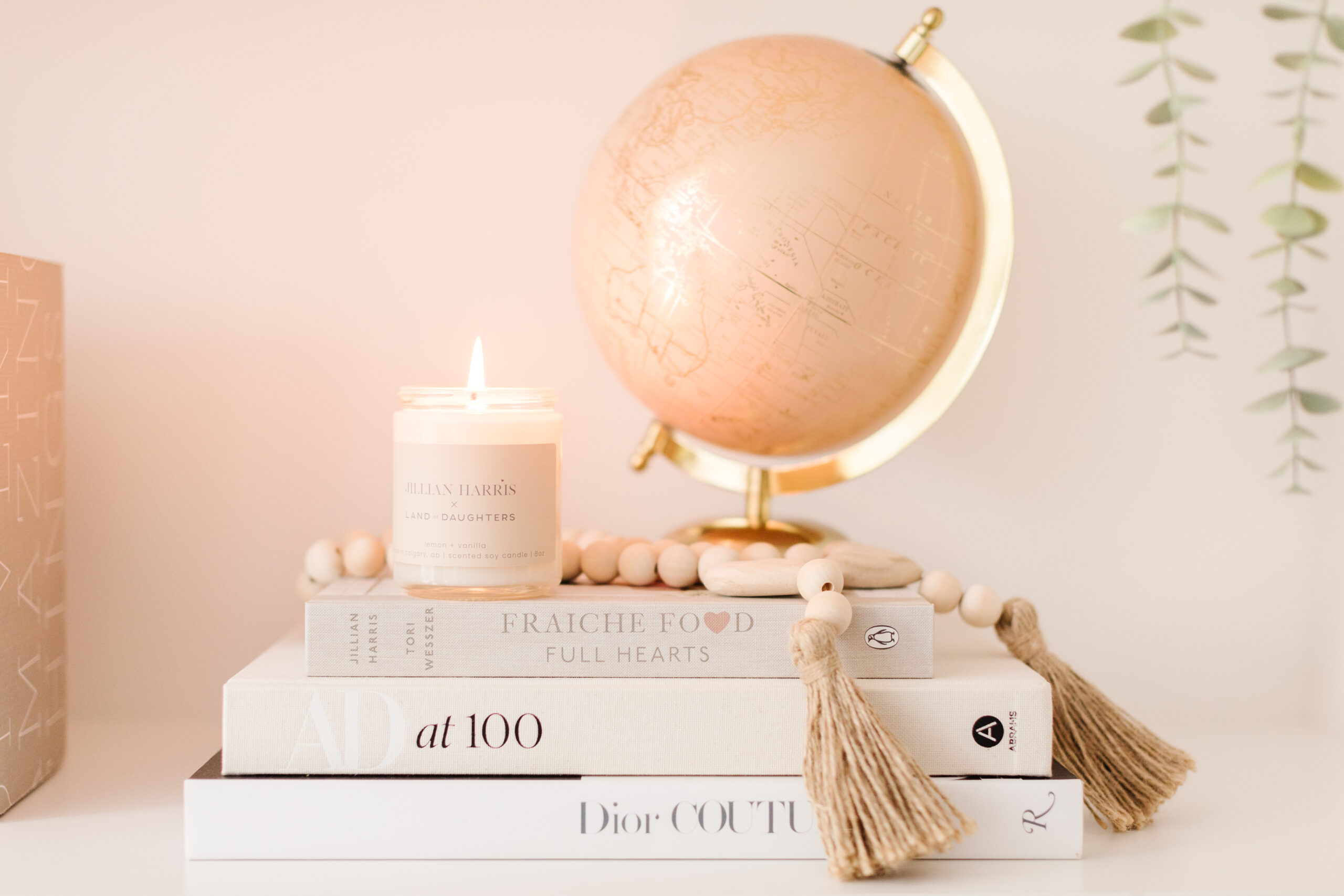 Jillian Harris' office shelf with a candle from Land of Daughters, a product featured in The Jilly Academy Box. Staged with a stack of books, prayer beads, and a globe.