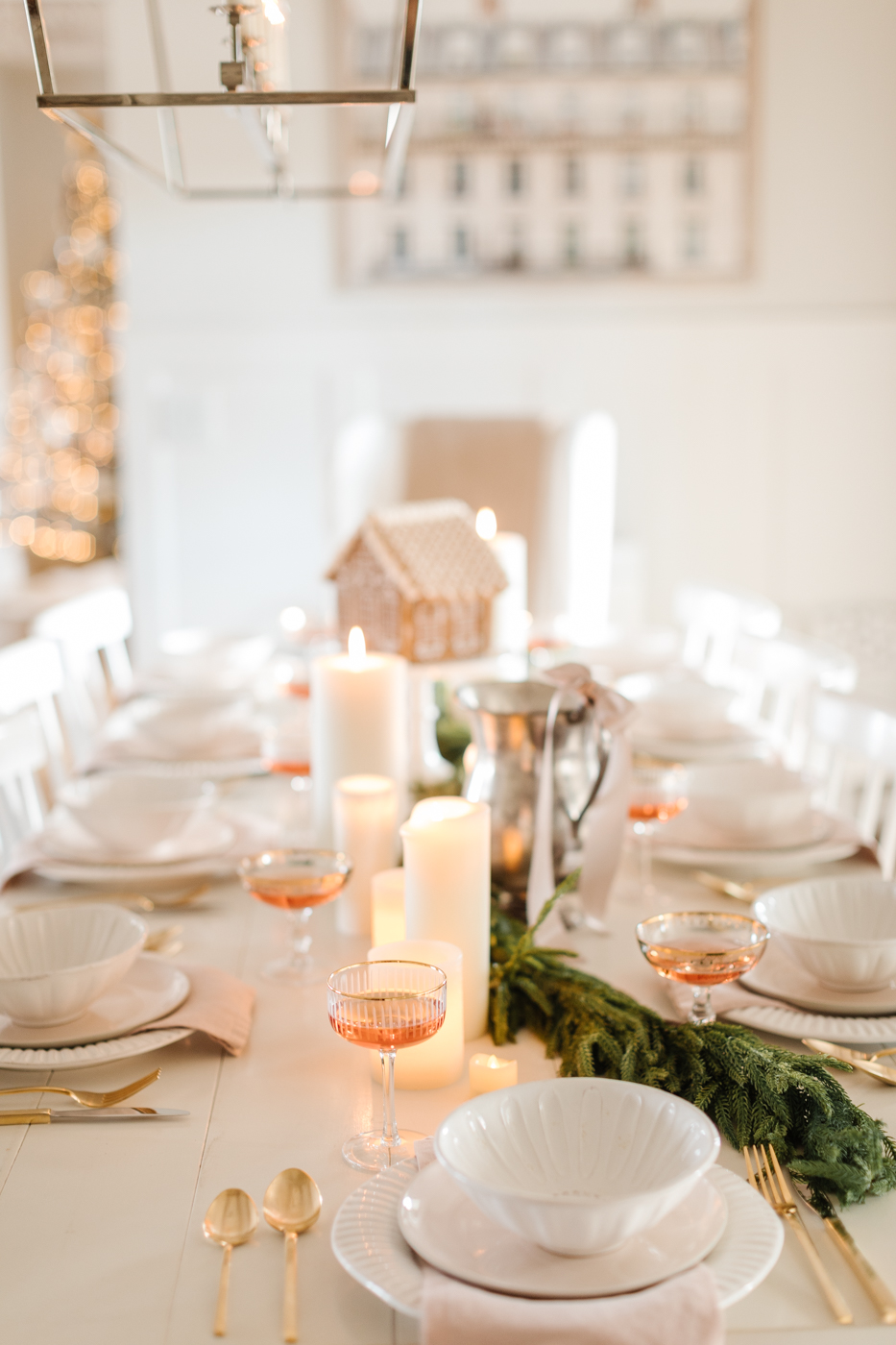 Table setting, gold rimmed glasses and cream plates with a garland running through the center holiday decor