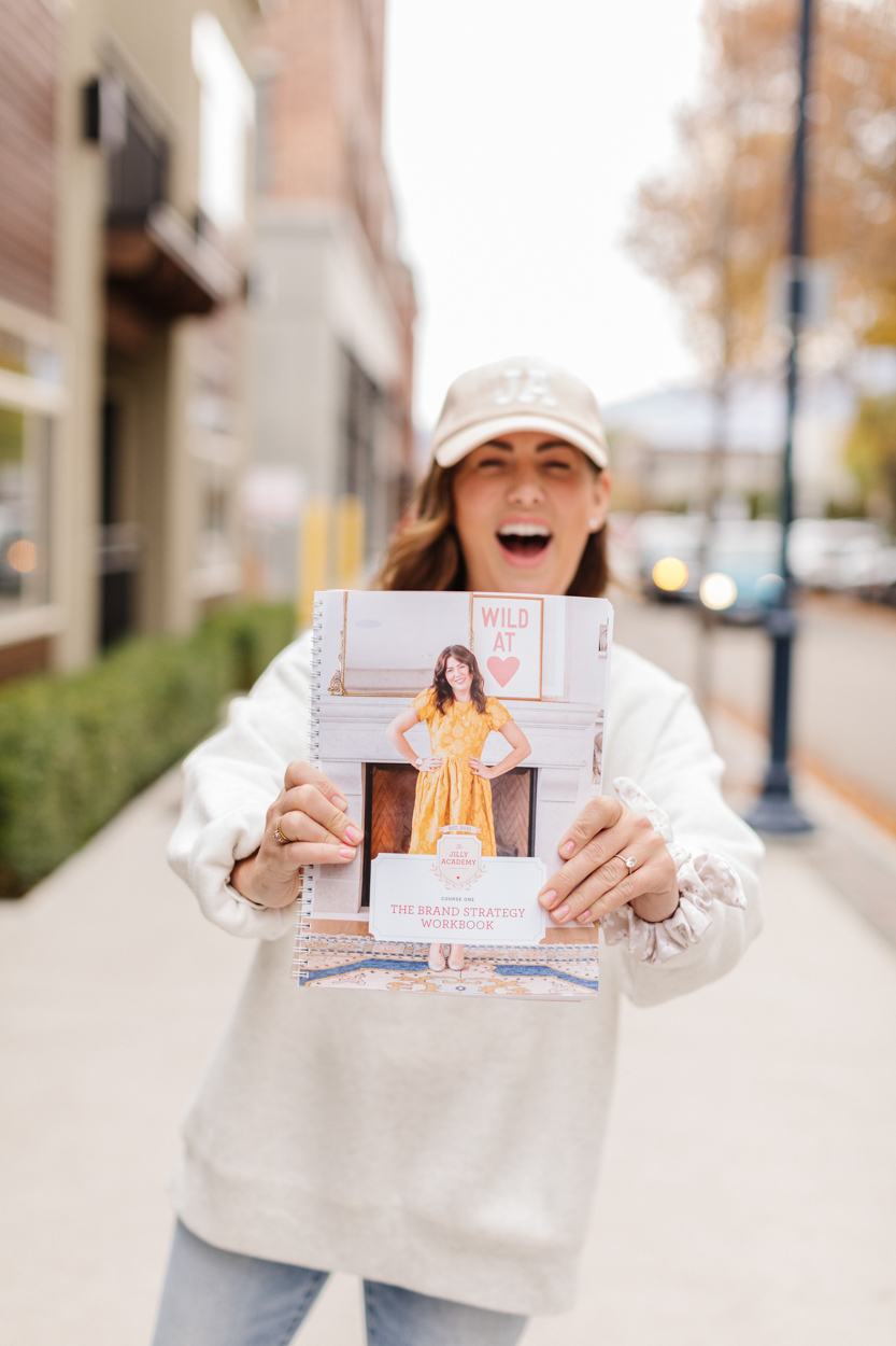 Jillian Harris holding The Jilly Academy Workbook wearing swag from The Jilly Academy Box. 