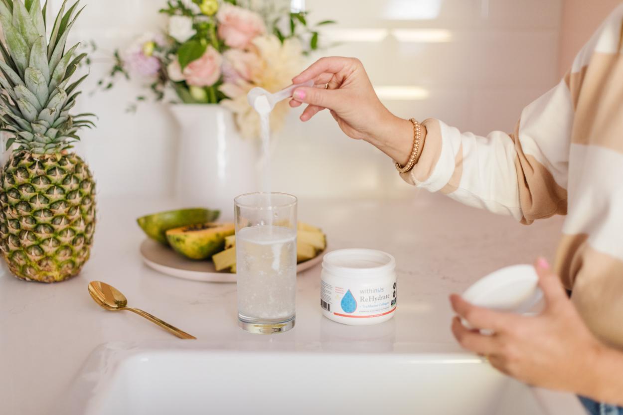 Jillian Harris pouring withinUs ReHydrate into a glass of water, a product featured in The Jilly Academy Box. 