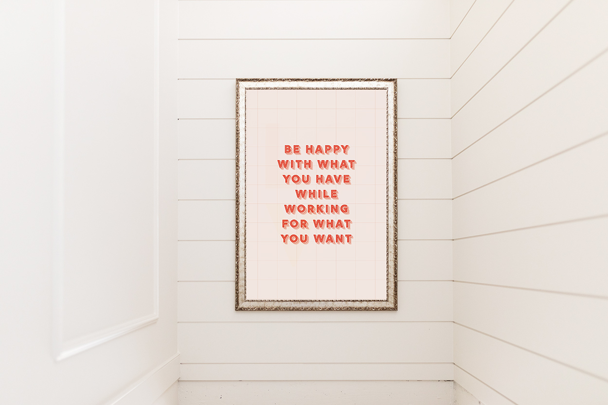 Jillian Harris' office wall showing the new digital prints featured in our Campus Store. A gold frame holds the "Be happy with what you have while working for what you want" quote. 