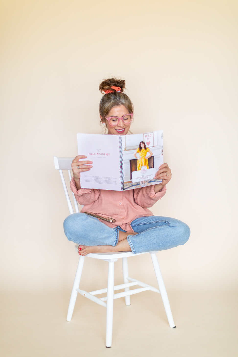 Jillian Harris sits on a chair holding The Jilly Academy Workbook available in The Campus Store. 