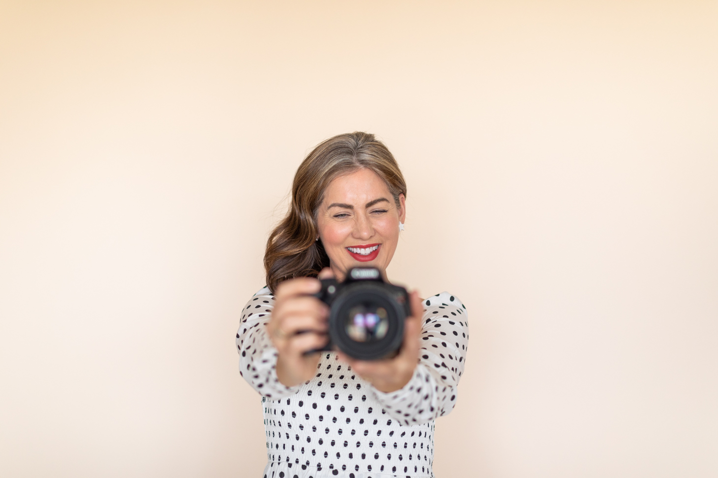 Jillian Harris wearing a black and white polka dot dress holding a camera up to take a video.