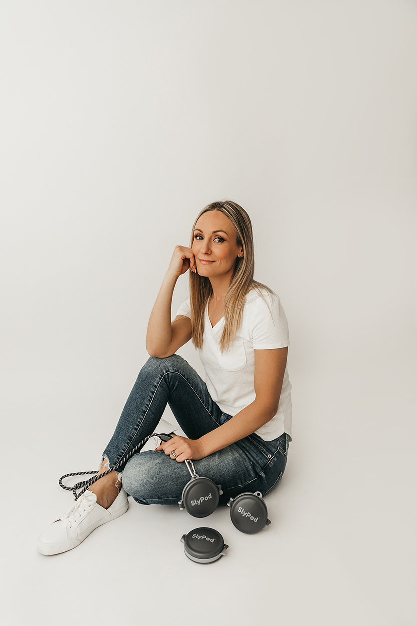 Jilly Academy Alumni member Nicole Duff sitting on a white backdrop wearing a white v-neck t-shirt, blue jeans and white sneakers. She is showcasing her product where she took one of her big risks on, SlyPod.