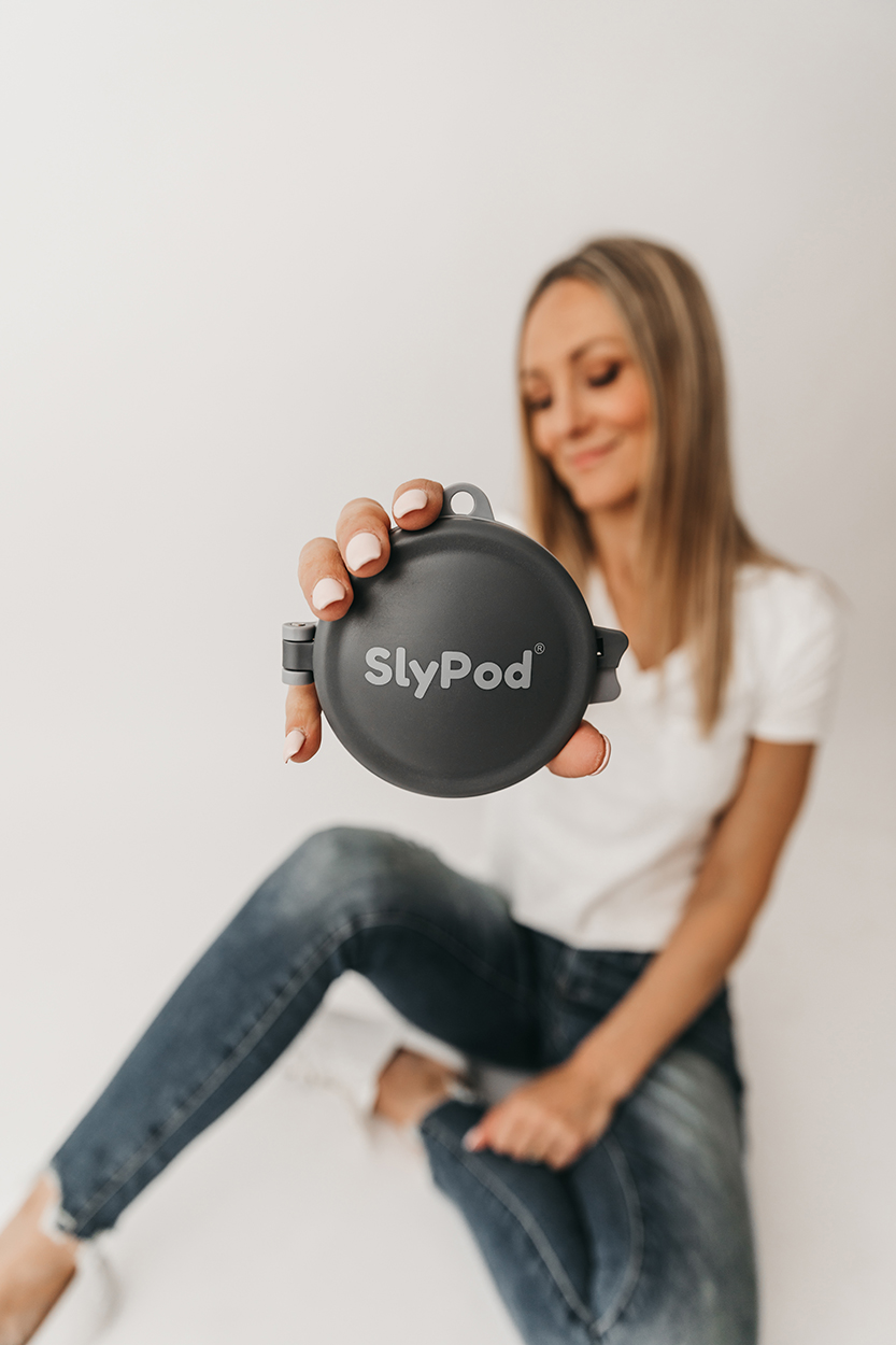 Jilly Academy Alumni member Nicole Duff sitting on a white background wearing blue jeans, a white v-neck shirt and white sneakers. She is holding the product where she took one of her big risks on, SlyPod.