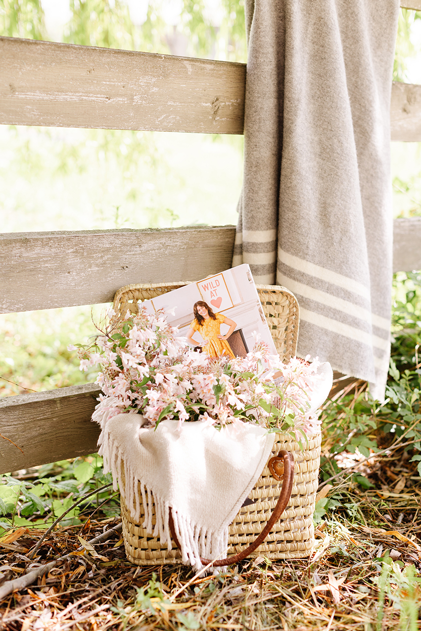 The Jilly Academy workbooks in a woven basket with flowers next to a blanket on the fence. The perfect online course to help you restart at any age. 