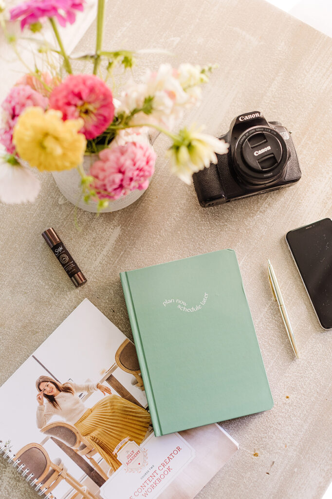 Overview shot of flatly of gift bag items: Later Media planner and Saje Wellness Roll-on. Complete with a Canon DSLR camera, Jilly Academy workbook, a gold pen and a phone.