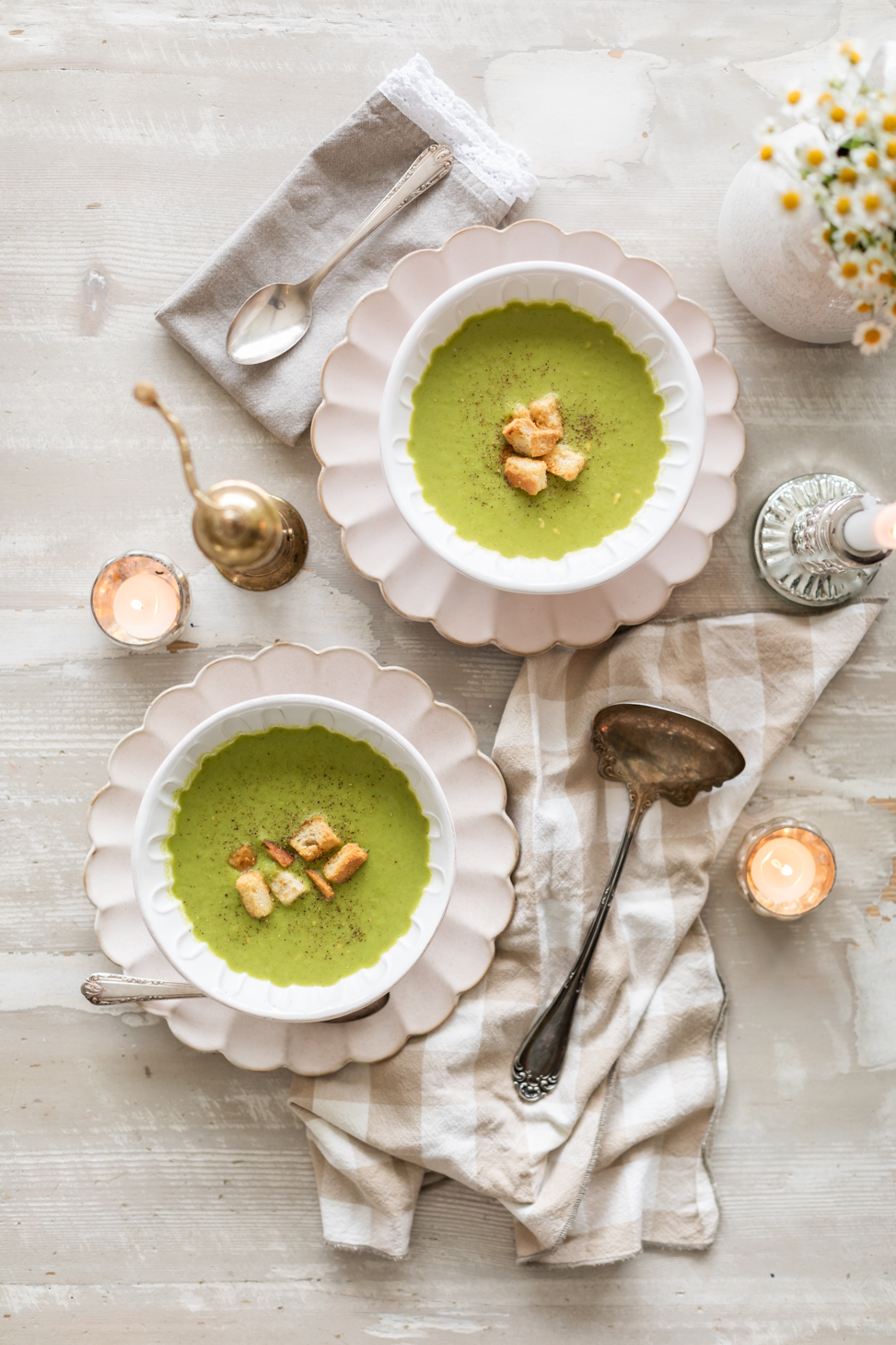 Jillian Harris's hearty green soup in a white bowl on a cement tabletop with small daisies in a vase