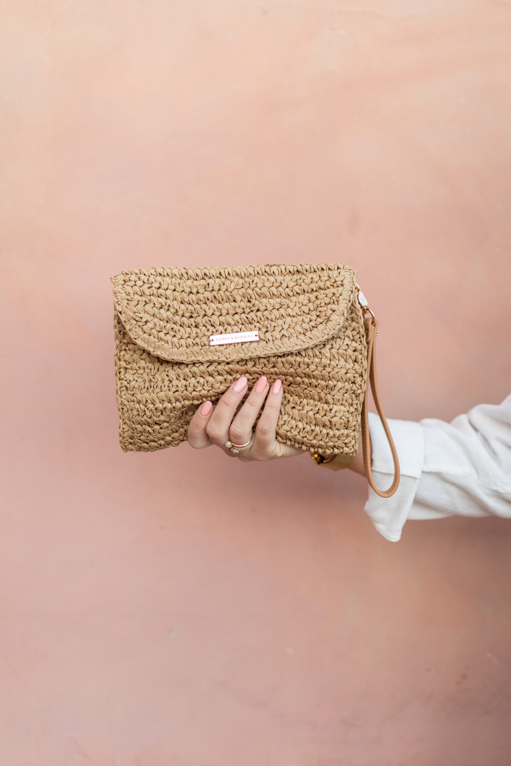 Poppy and peonies clutch held up in front of pink wall