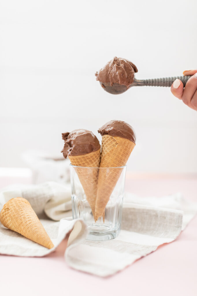 A hand scooping chocolate ice cream into waffle cones, highlighting Fraiche Food, Fuller Hearts cookbook desserts