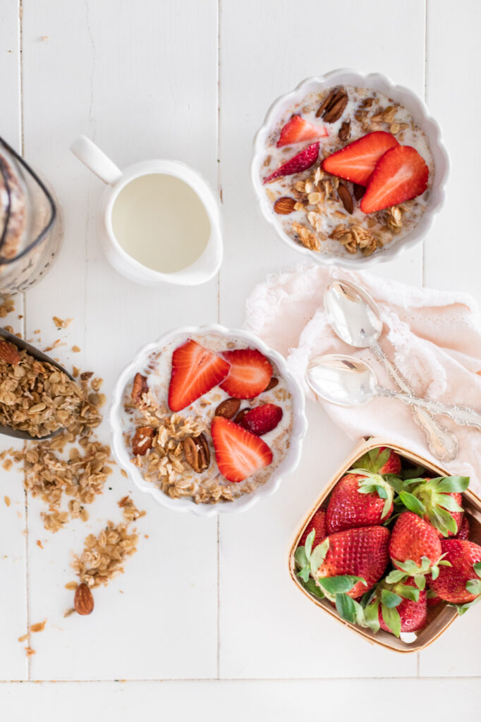 a top-down view of a breakfast table with bowls of granola topped with strawberries and a bowl of whole strawberries beside