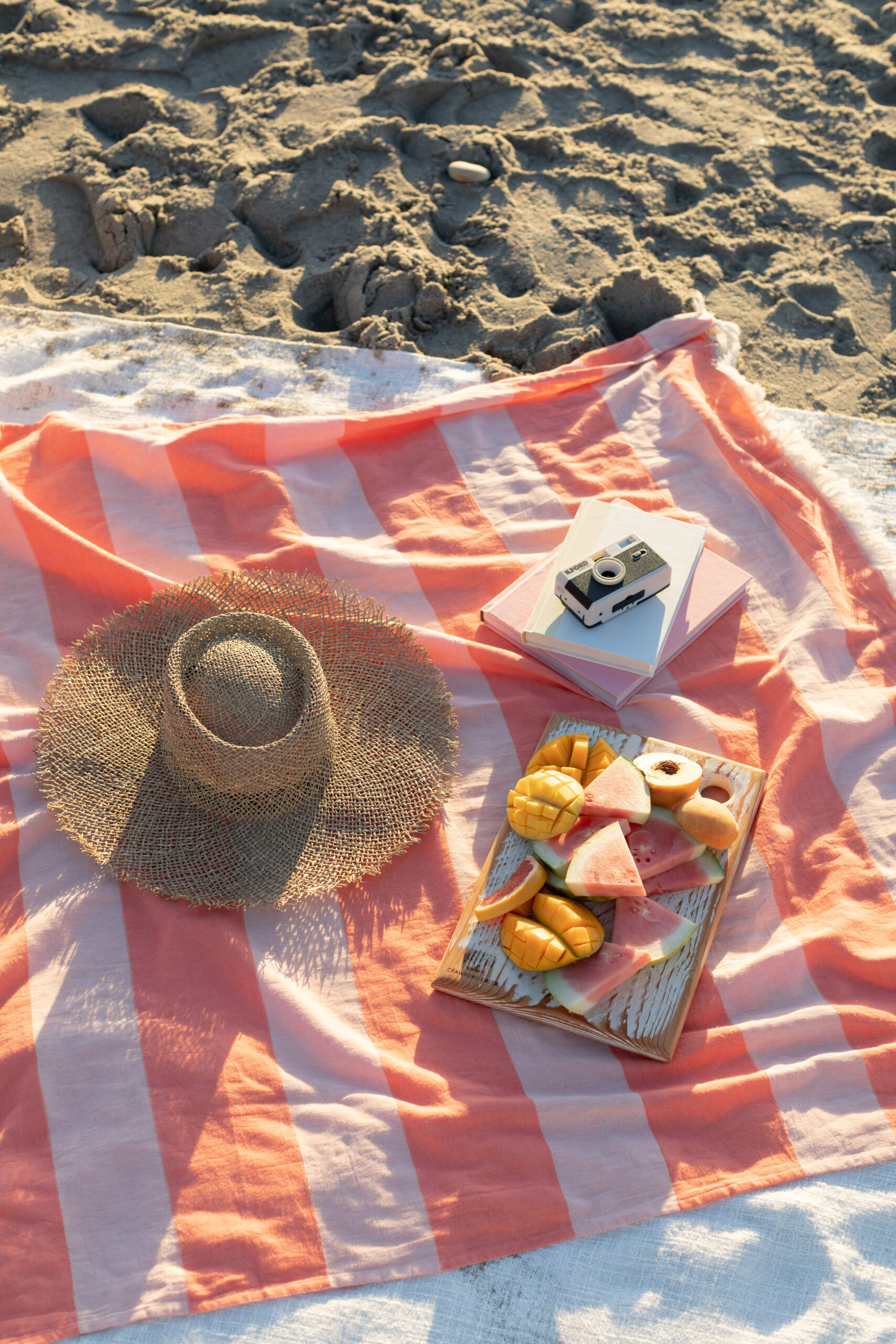 Orange striped tofino towel co throw with fruit, books and a hat on it