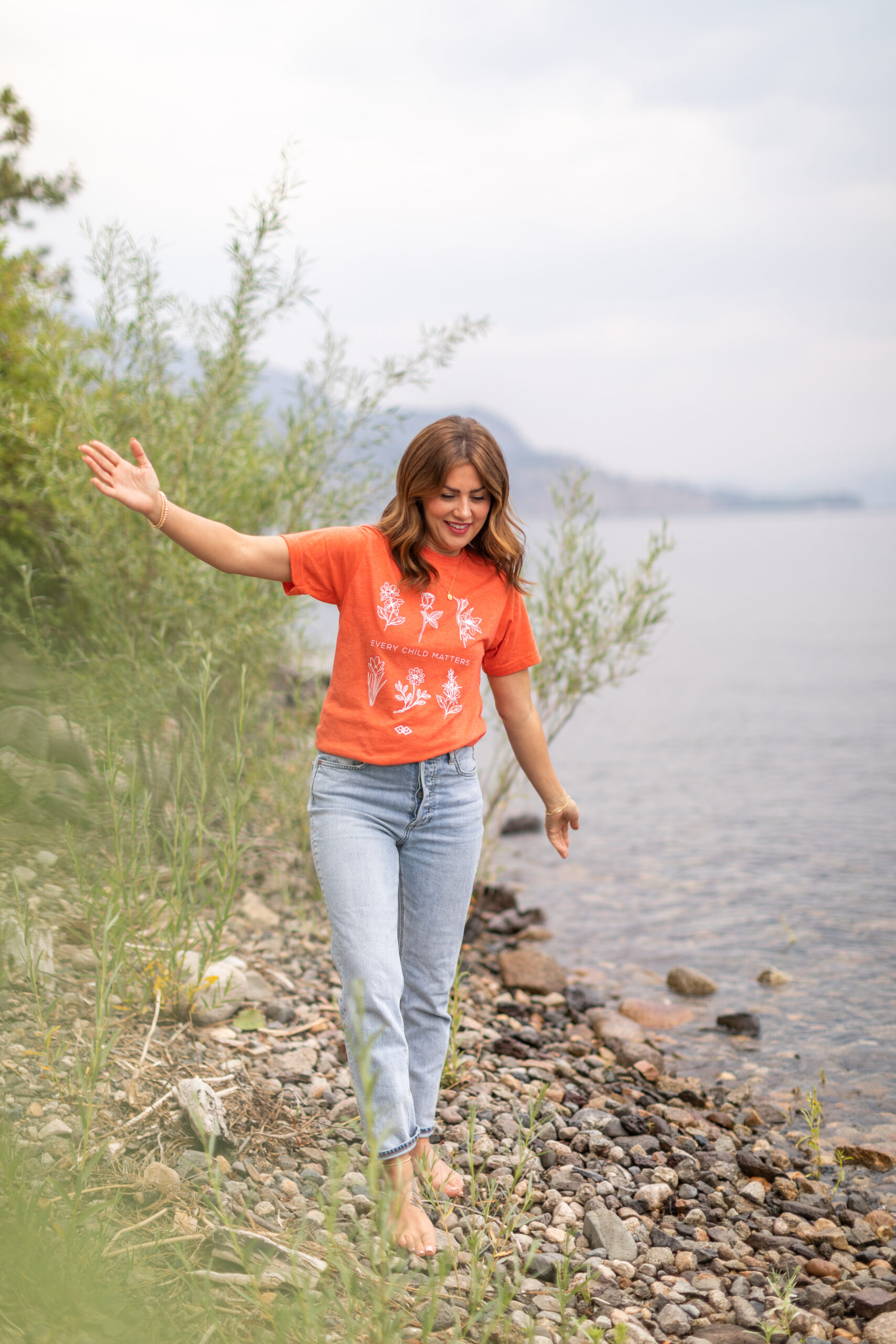 Jillian wearing the Jilly Box x Awasis Orange Shirt in front of the lake 