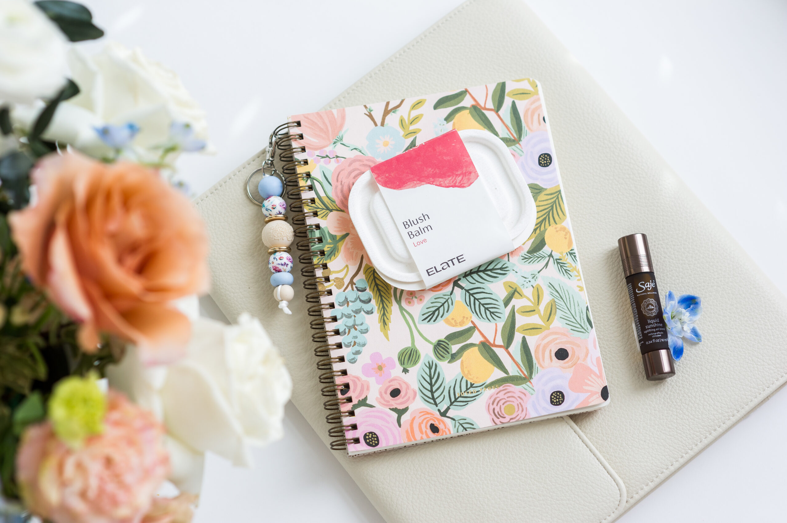 Elate Blush, a keychain and Saje roll-on placed on top of a notebook.