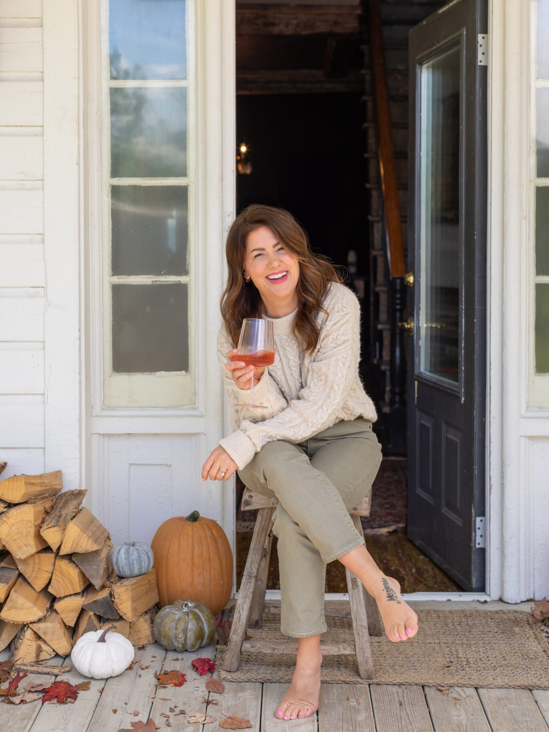 Jillian Harris wearing the 2024 Jillian Harris x Joe Fresh x Life At Home™ Fall Collection holding a pink glass of wine, sitting on the front porch. 