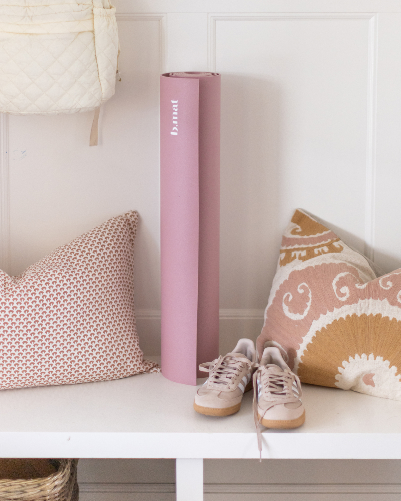 A yoga mat in a mud room by two pillows, running shoes, and a backpack. 