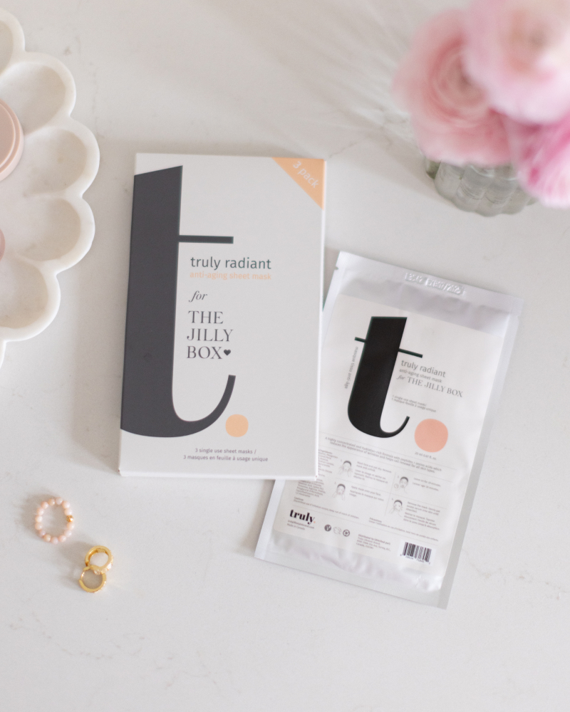 A package of the Truly sheet masks on a table by flowers, earrings, and a scalloped bowl. 