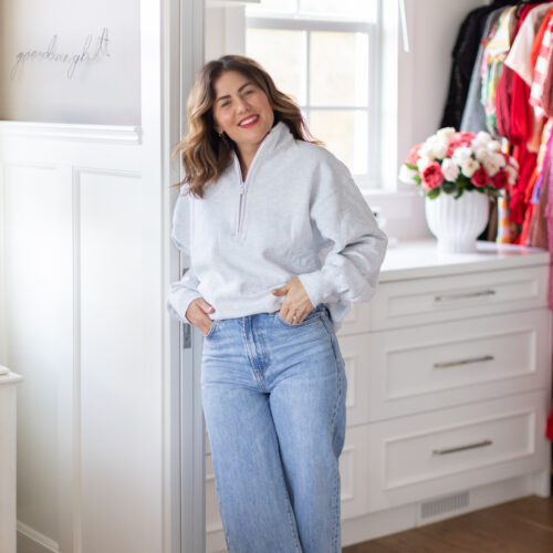 Jillian standing in her closet wearing a grey crewneck and jeans.
