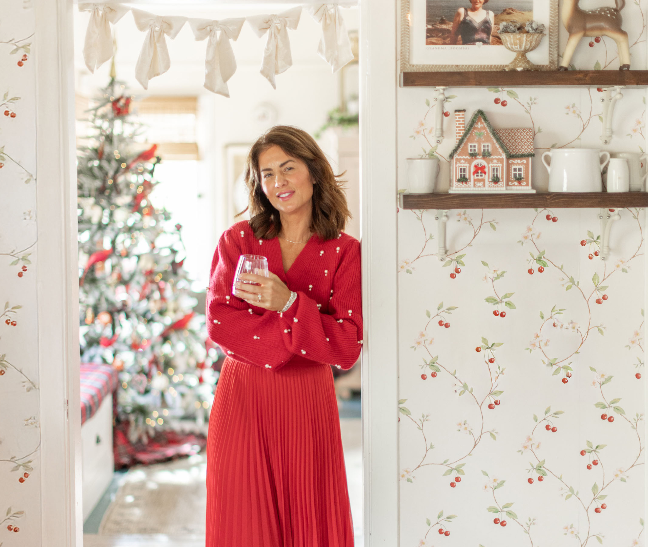 Jillian Harris dressed in festive red, holding a glass. A Christmas Tree show in the background.