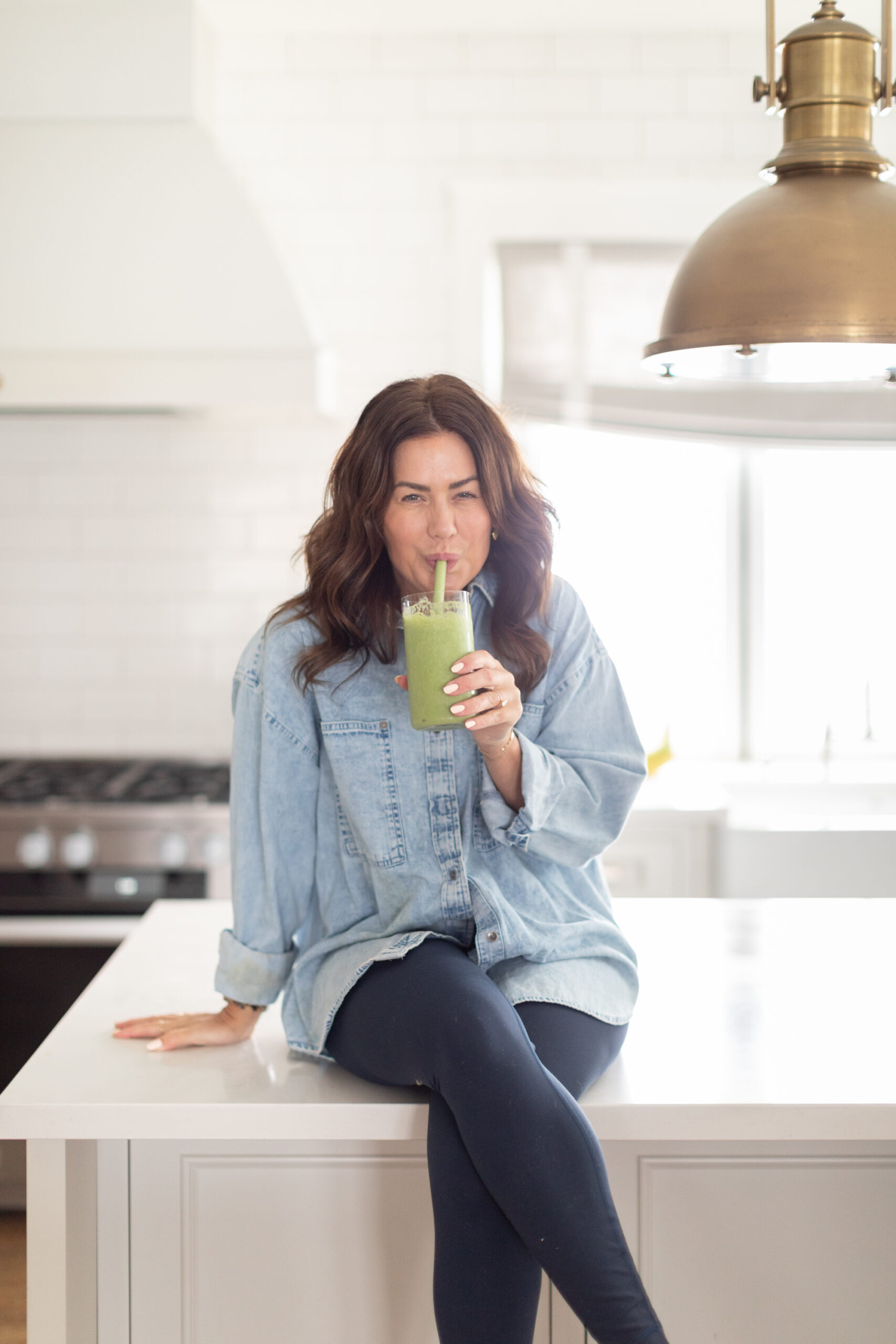 Jillian sitting on kitchen counter drinking a green juice